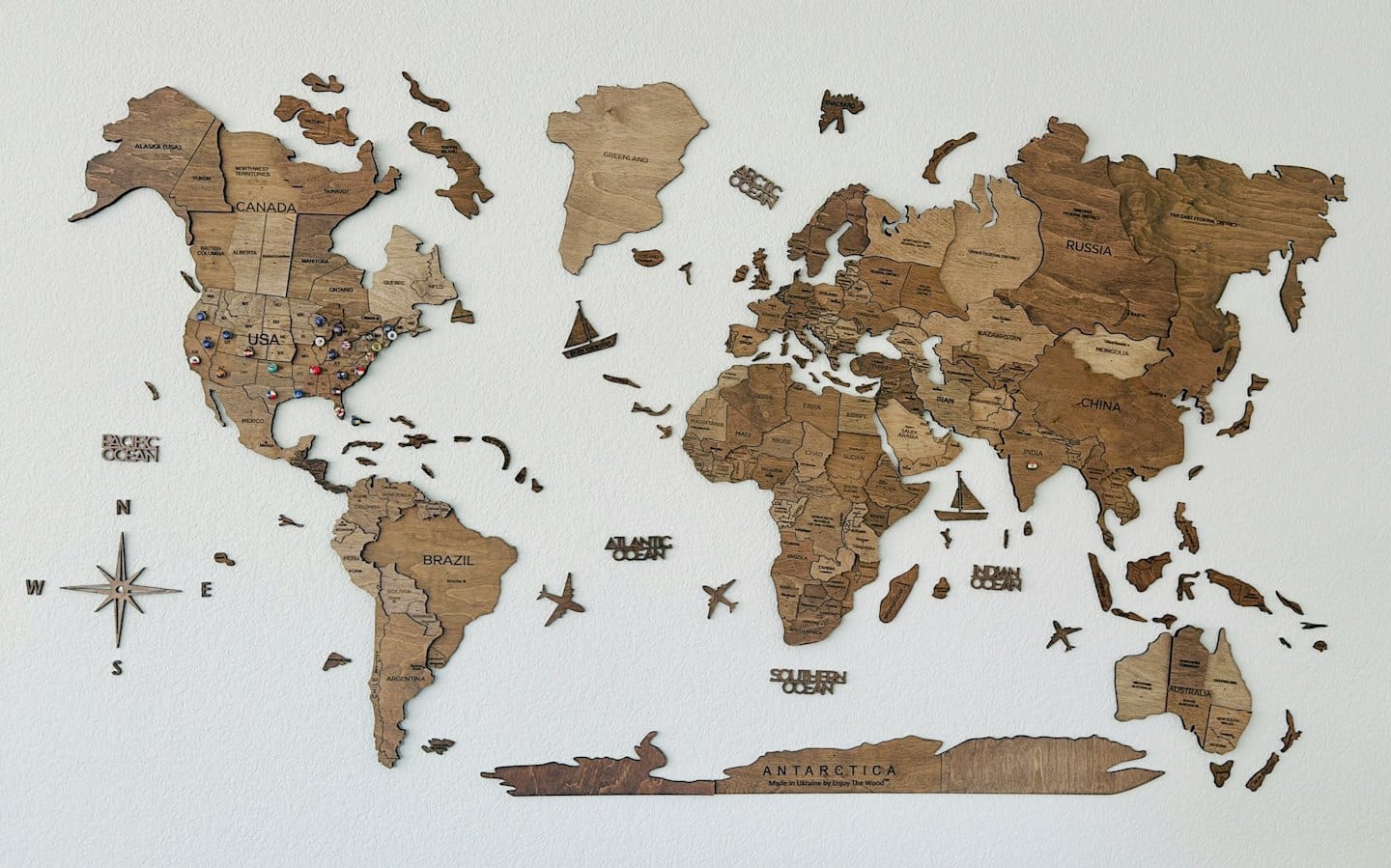 Drevená mapa sveta na bielej stene s pripnutými špendlíkmi v Severnej Amerike.